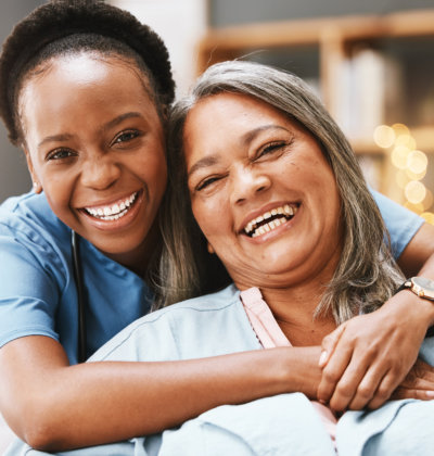 female caregiver happily hugging elderly woman